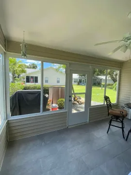Enclosed porch with large windows, gray tile floor, and a chair facing a sunny backyard.