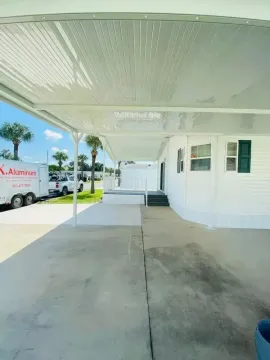 Covered driveway beside a white house, with concrete walkway, parked van, and bright sunny sky