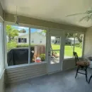 Screened porch with gray siding, sliding door, patio chair, and a view of a green backyard and neighboring houses