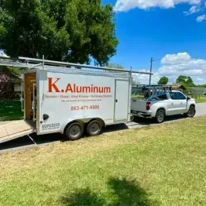 White K. Aluminum trailer hitched to a silver SUV on a sunny grassy roadside.