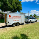 White K. Aluminum trailer hitched to a silver SUV on a sunny grassy roadside.