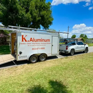White K. Aluminum trailer hitched to a silver SUV on a sunny grassy roadside.