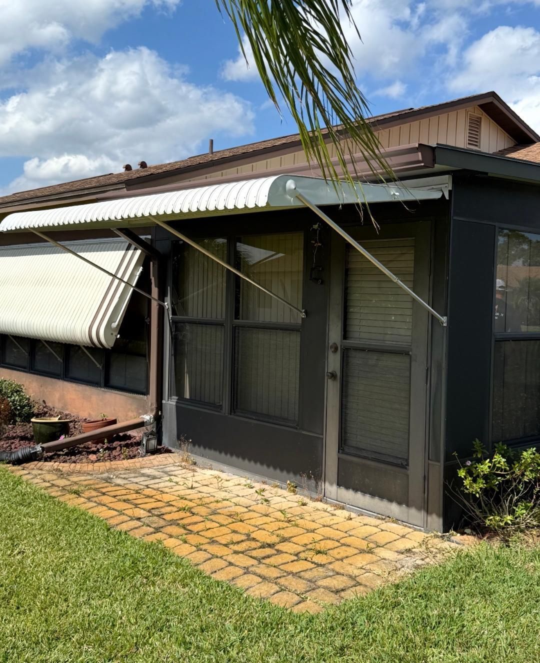 Two men inspect an awning outside a sunlit suburban home