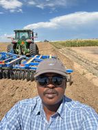 Man in sunglasses, baseball cap in field with tractor.