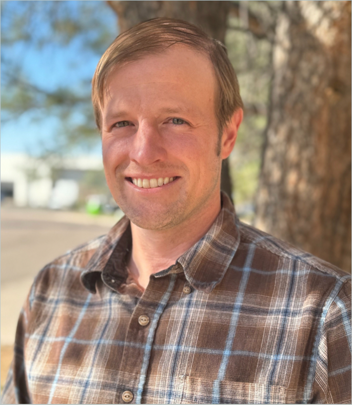 Smiling man with light hair, brown plaid shirt, outdoors.