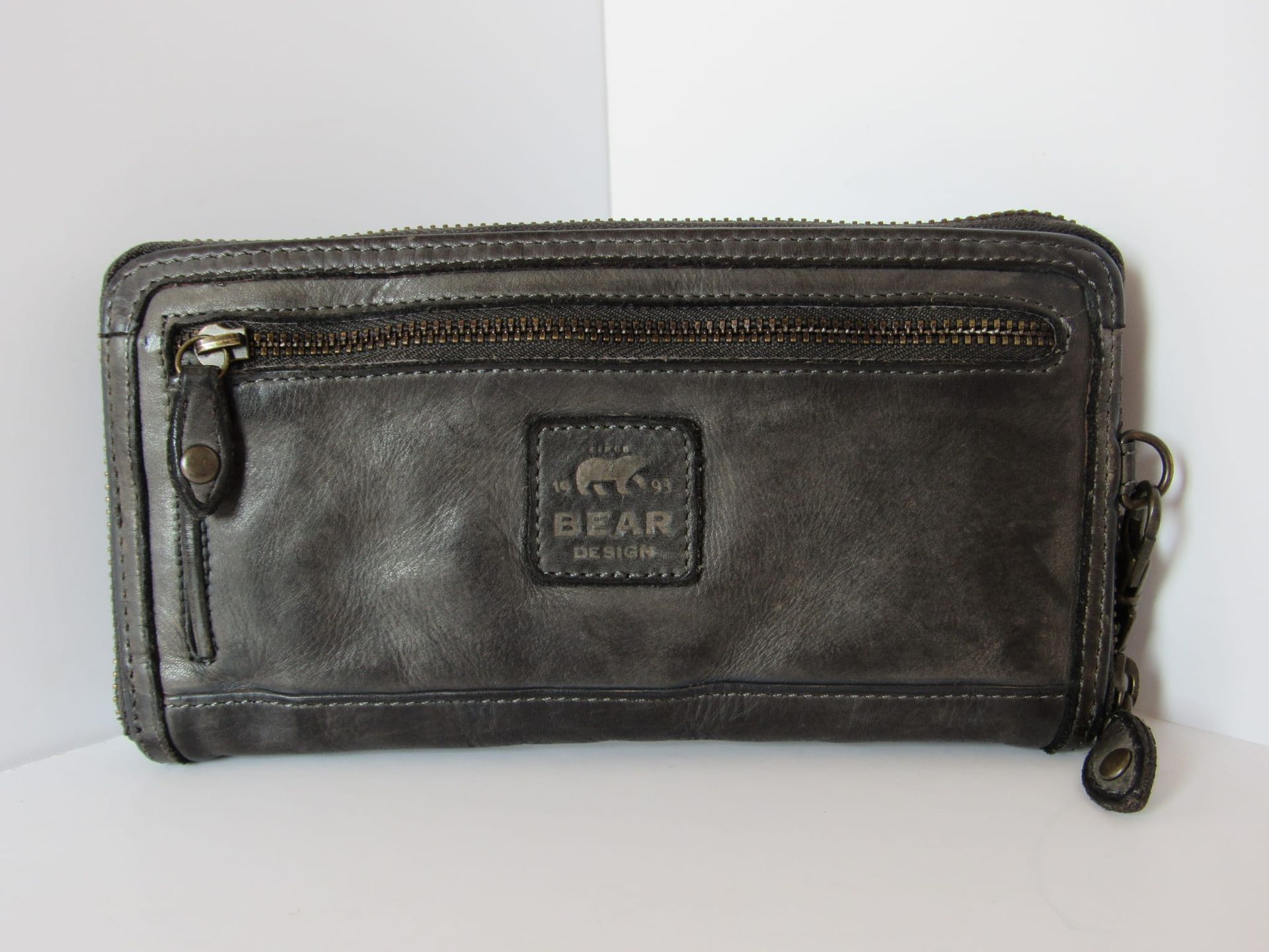 Donkergrijze geweven leren clutch met polsbandje, schuin geplaatst op een witte achtergrond.