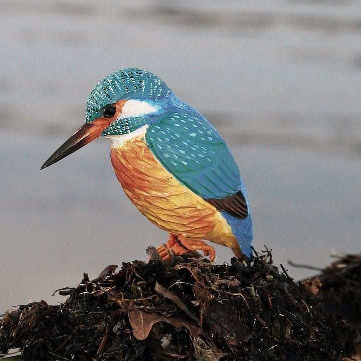Een houten ijsvogel, gebeeldhouwd en zittend op een kleine boomstronk, in levendige kleuren.