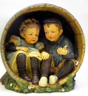 Twee kinderen zitten in een ton en kijken elkaar aan. Ze dragen allebei vintage kleding en hebben roze wangen.