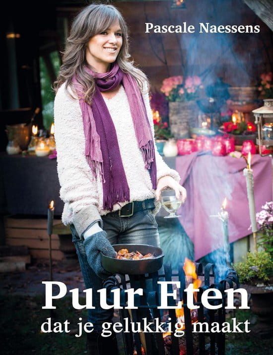 Vrouw met eten in haar handen, lachend, bij een vuur en een gedekte tafel buiten. Boektitel: Puur Eten.
