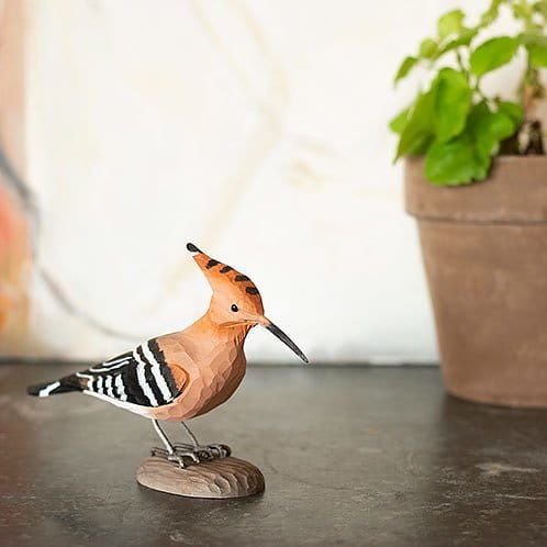 Houten beeldje van een hop met een opstaande kuif, zwart-wit gestreepte vleugels en zittend op een stenen voetstuk.