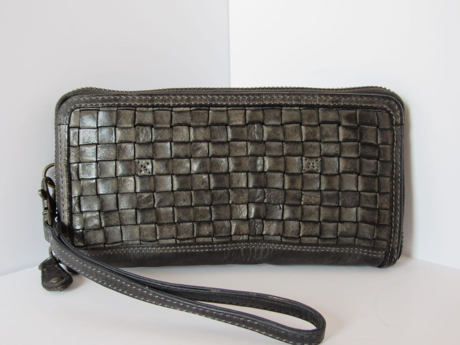 Donkergrijze geweven leren clutch met polsbandje, schuin geplaatst op een witte achtergrond.