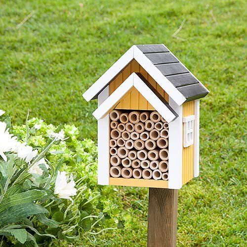 Geel-wit houten insectenhuis met een grijs dak, gevuld met bamboebuizen.