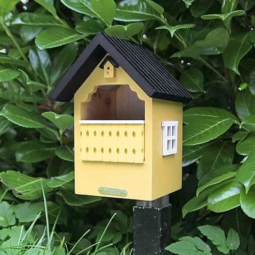 Geel vogelhuisje met een zwart dak en een veranda.