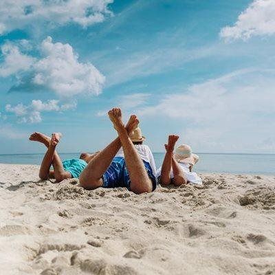 People relaxing on a sandy beach, with blue skies and ocean visible.