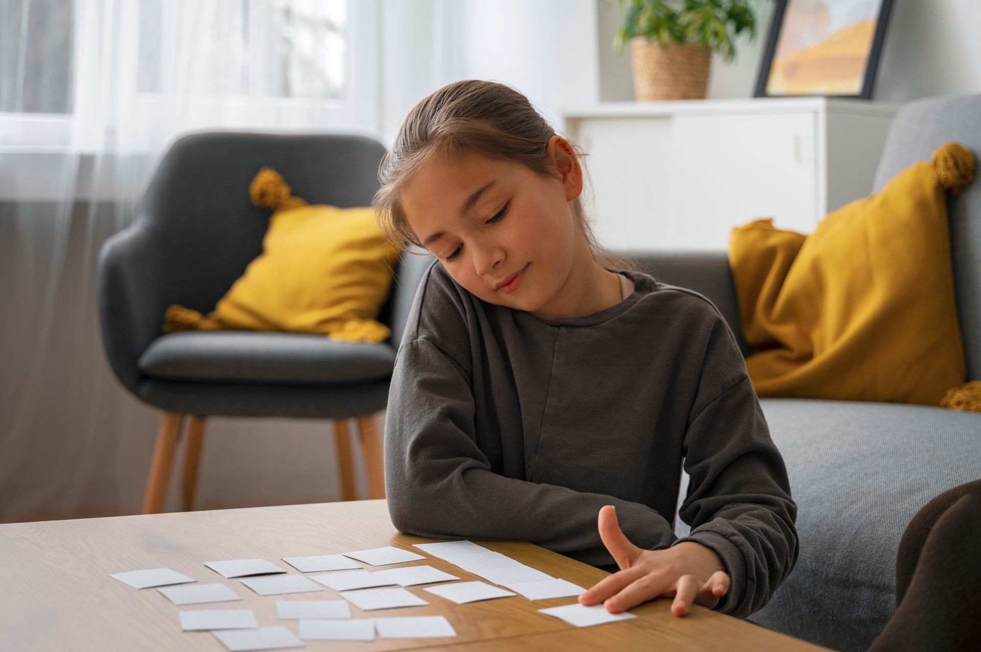 A person sits at a wooden table, concentrating while interacting with a grid of small, blank white cards in a home setting.