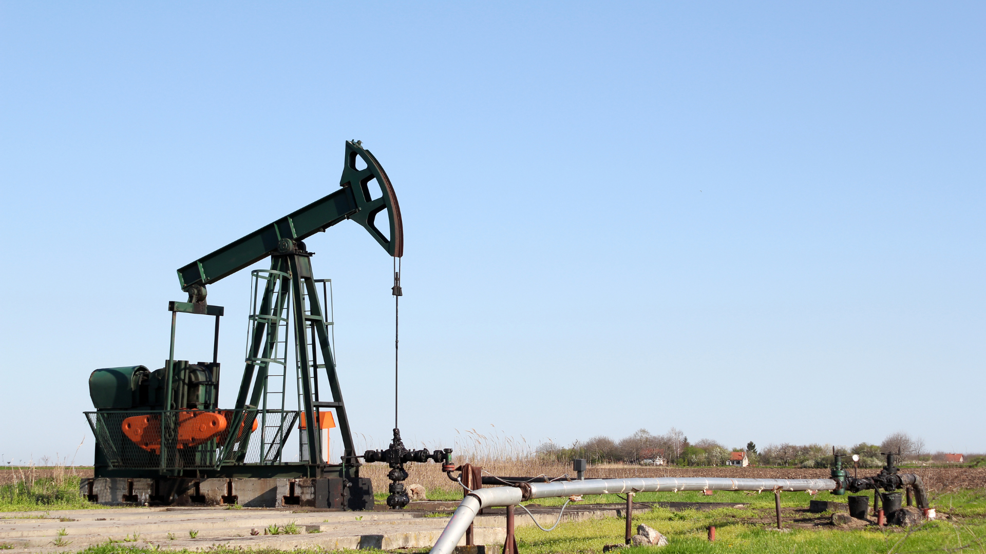 An oil pump is sitting in the middle of a grassy field.