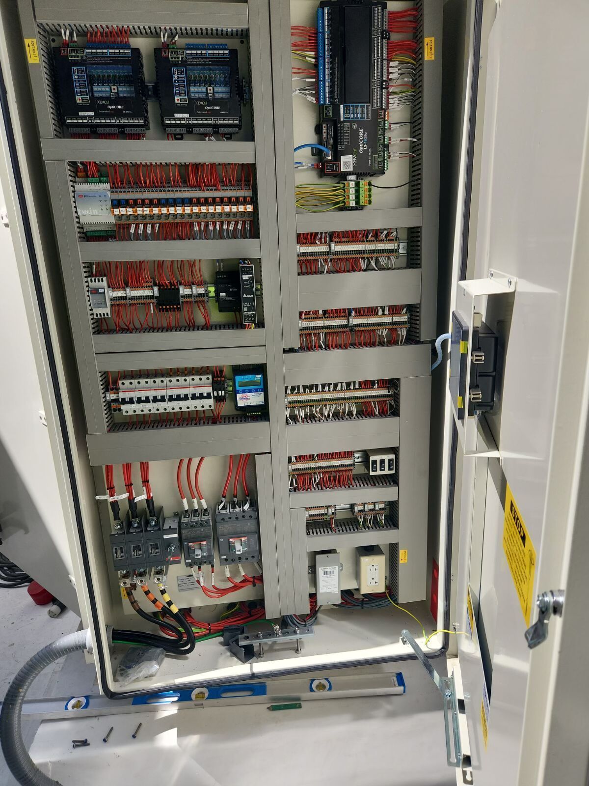 Open electrical control cabinet with wiring, circuit modules, and relays inside a white enclosure.