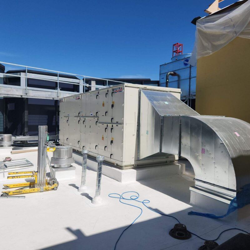 Rooftop HVAC equipment and silver ductwork on a white industrial roof under a clear blue sky.