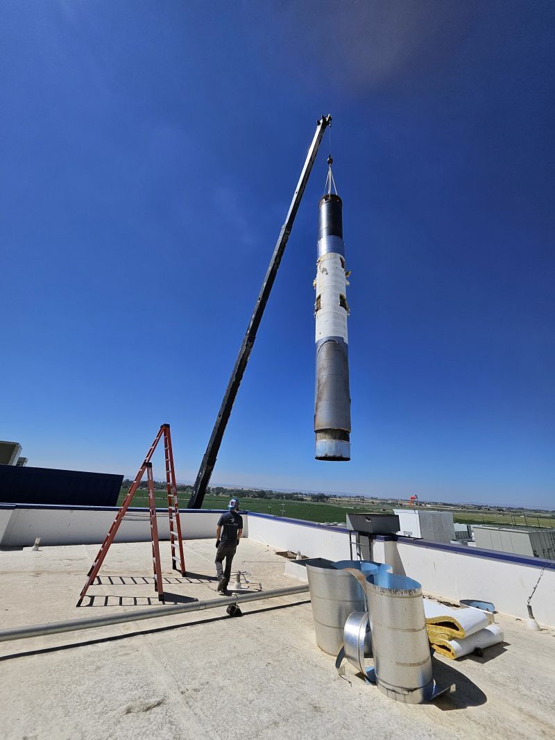 Rocket stage being lifted by crane on a rooftop under a clear blue sky