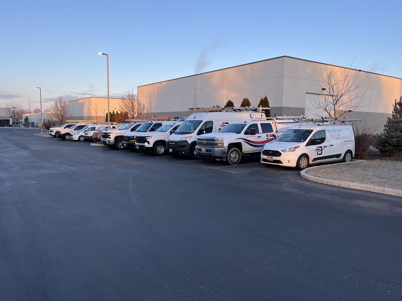 Row of white trucks parked beside a beige industrial building at dusk