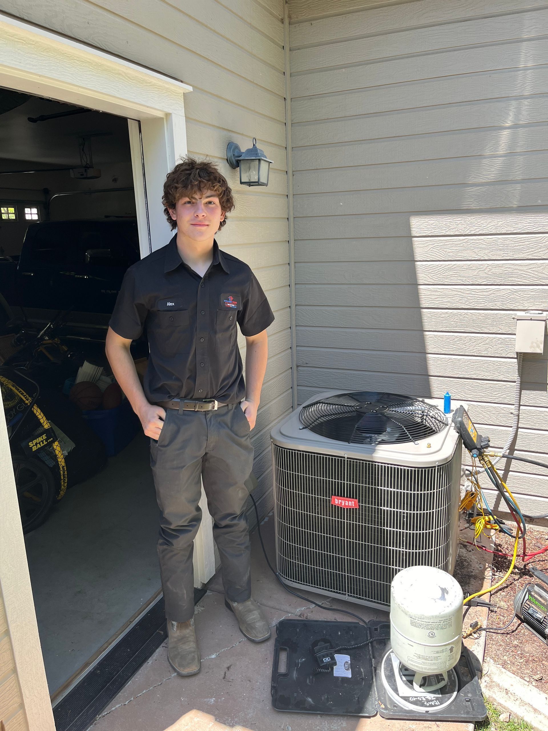 Person standing in a garage doorway beside an outdoor HVAC unit and a small propane tank