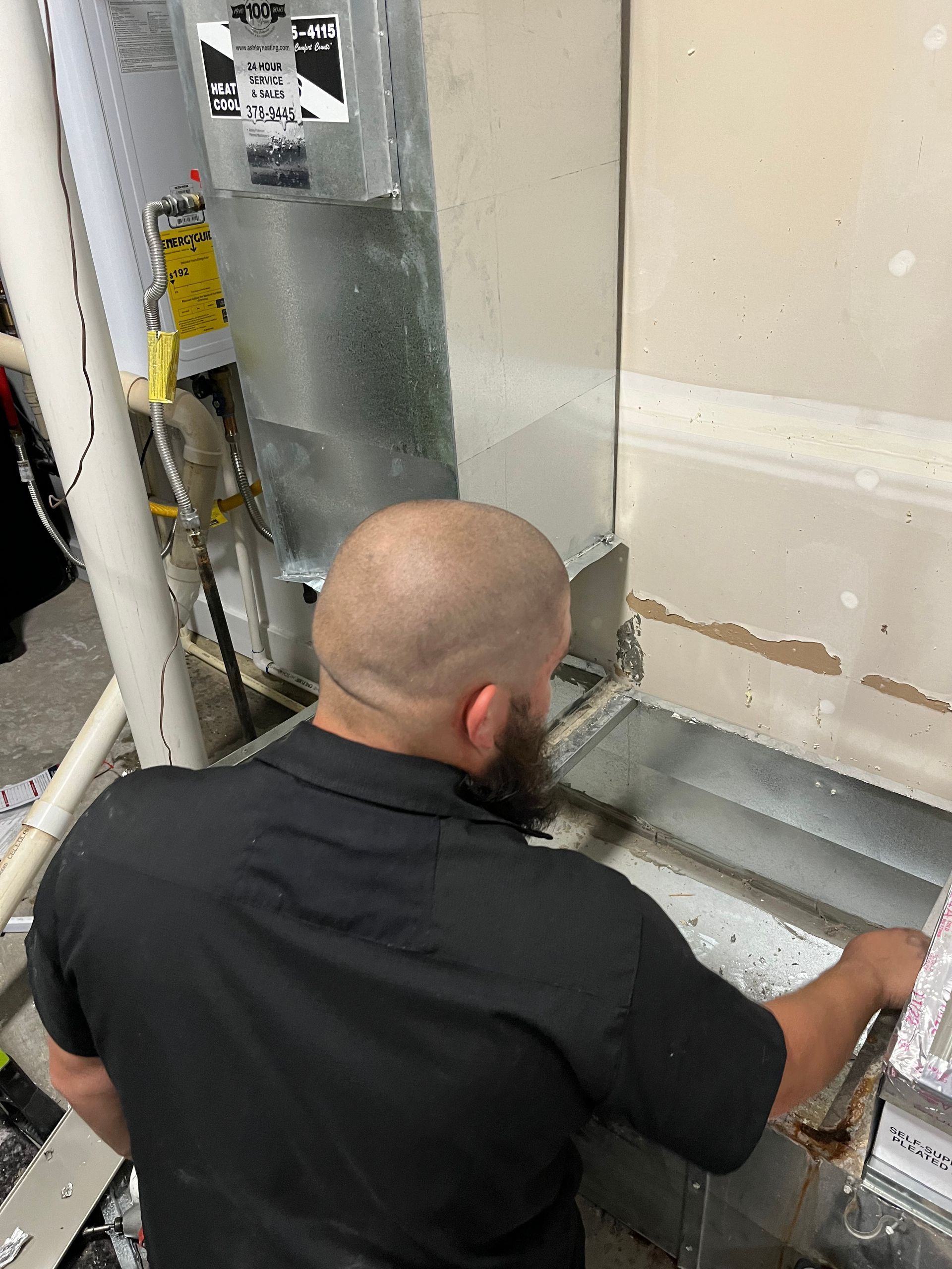 Technician working on HVAC ductwork beside a wall in a utility room