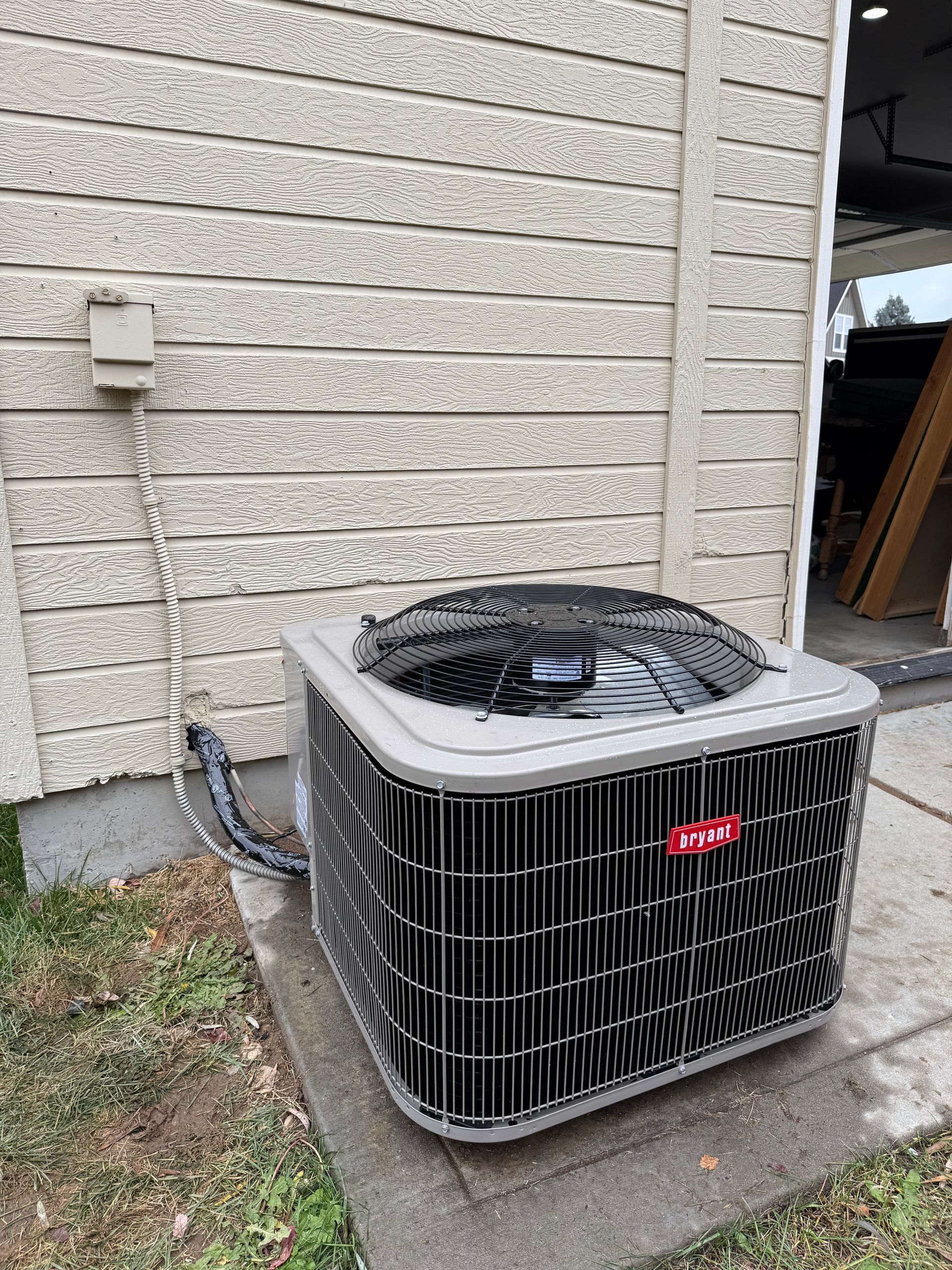 Outdoor air conditioner unit beside a house wall on a concrete pad with a hose attached