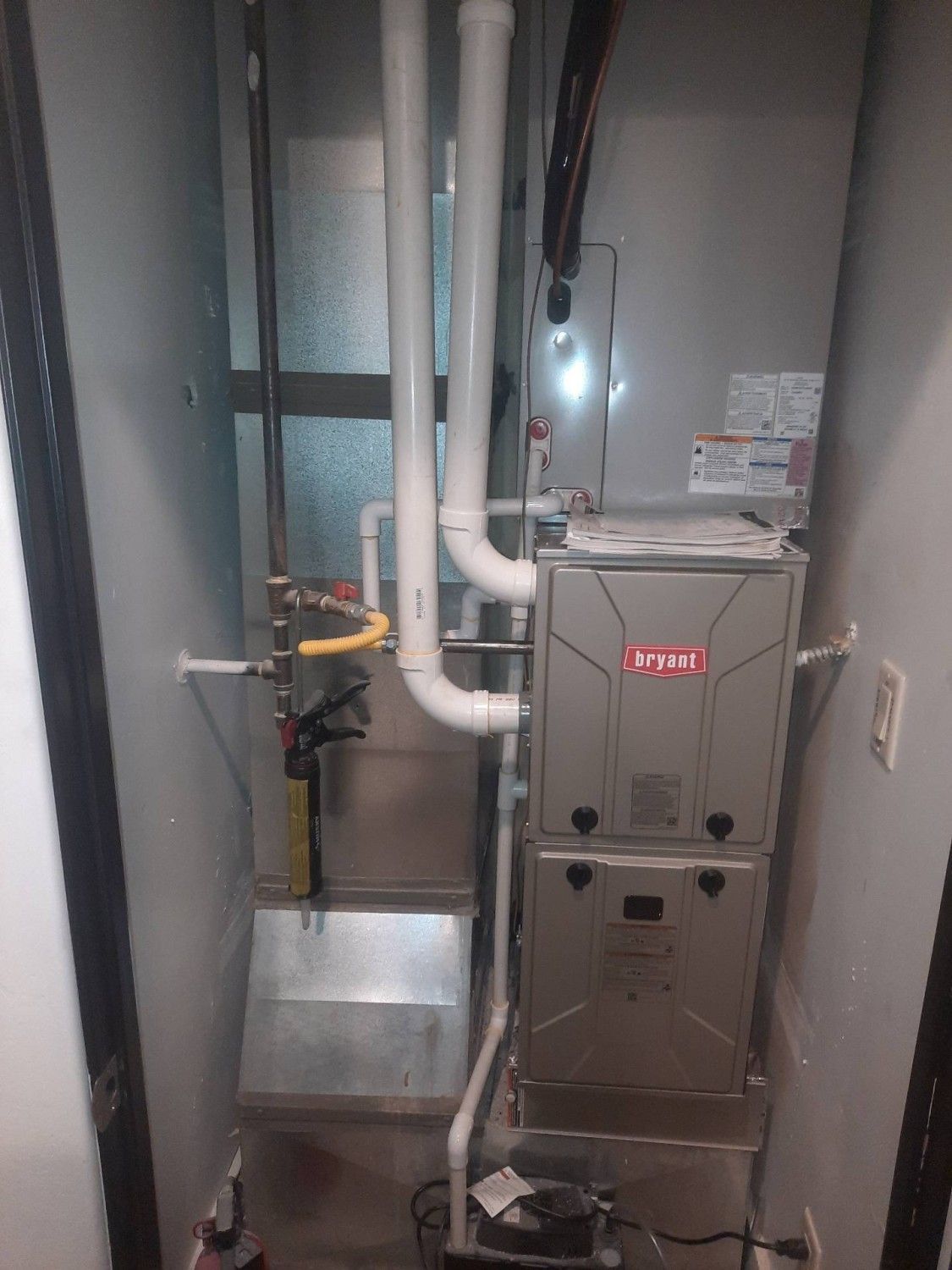 Utility closet with HVAC furnace, white pipes, and ductwork in a narrow gray room.