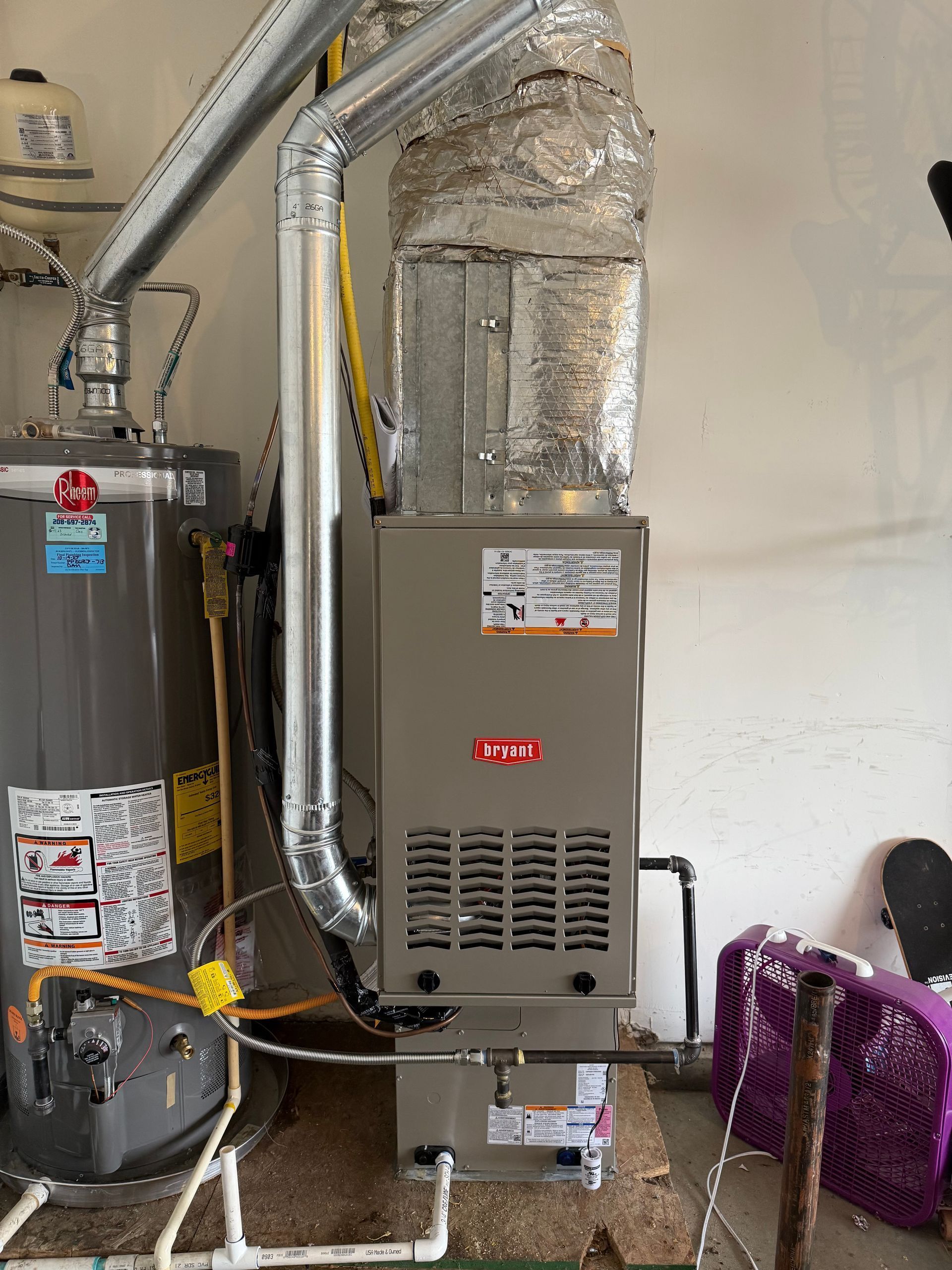 Furnace and water heater in a utility room with exposed ductwork and pipes.