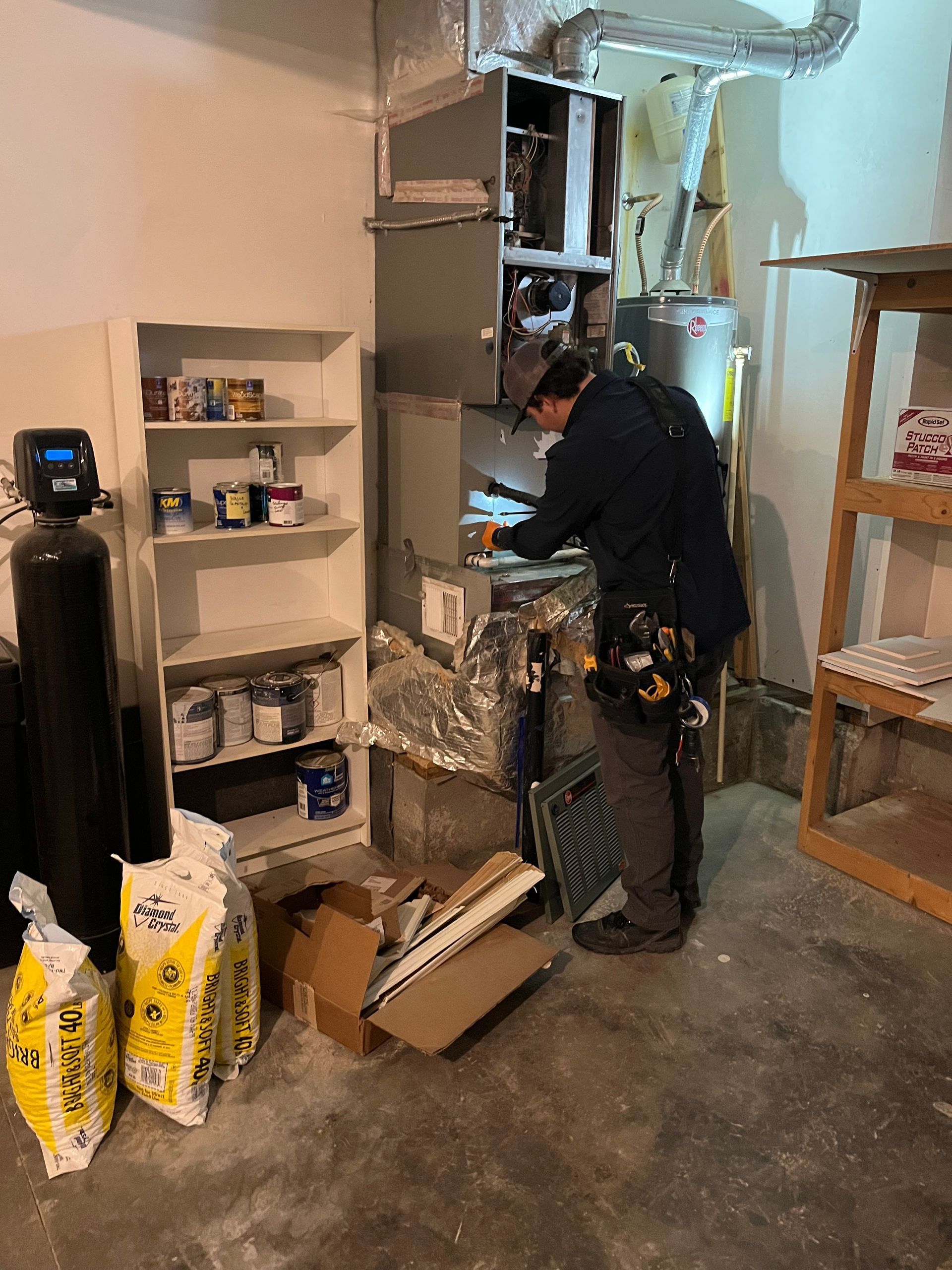 Worker inspecting equipment in an industrial room beside shelves and stacked bags