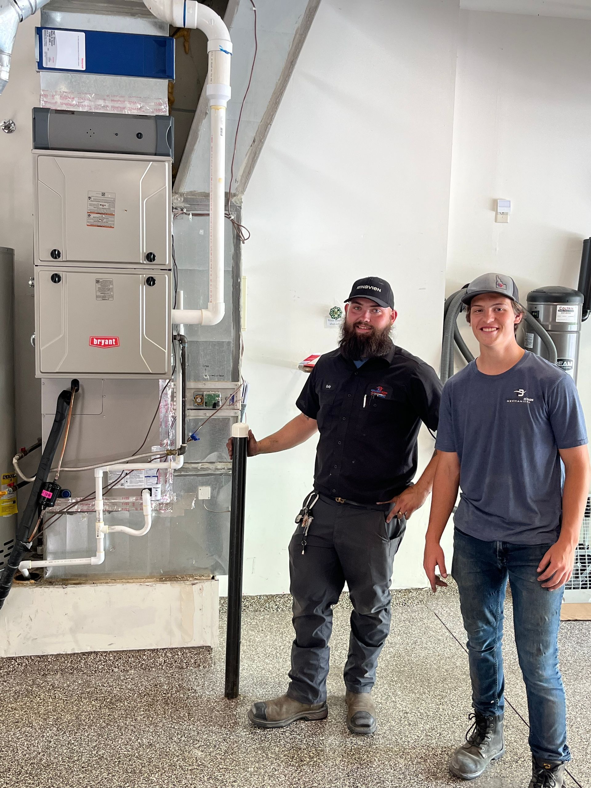 Two workers standing beside a wall-mounted electrical panel and exposed wiring in a utility room.