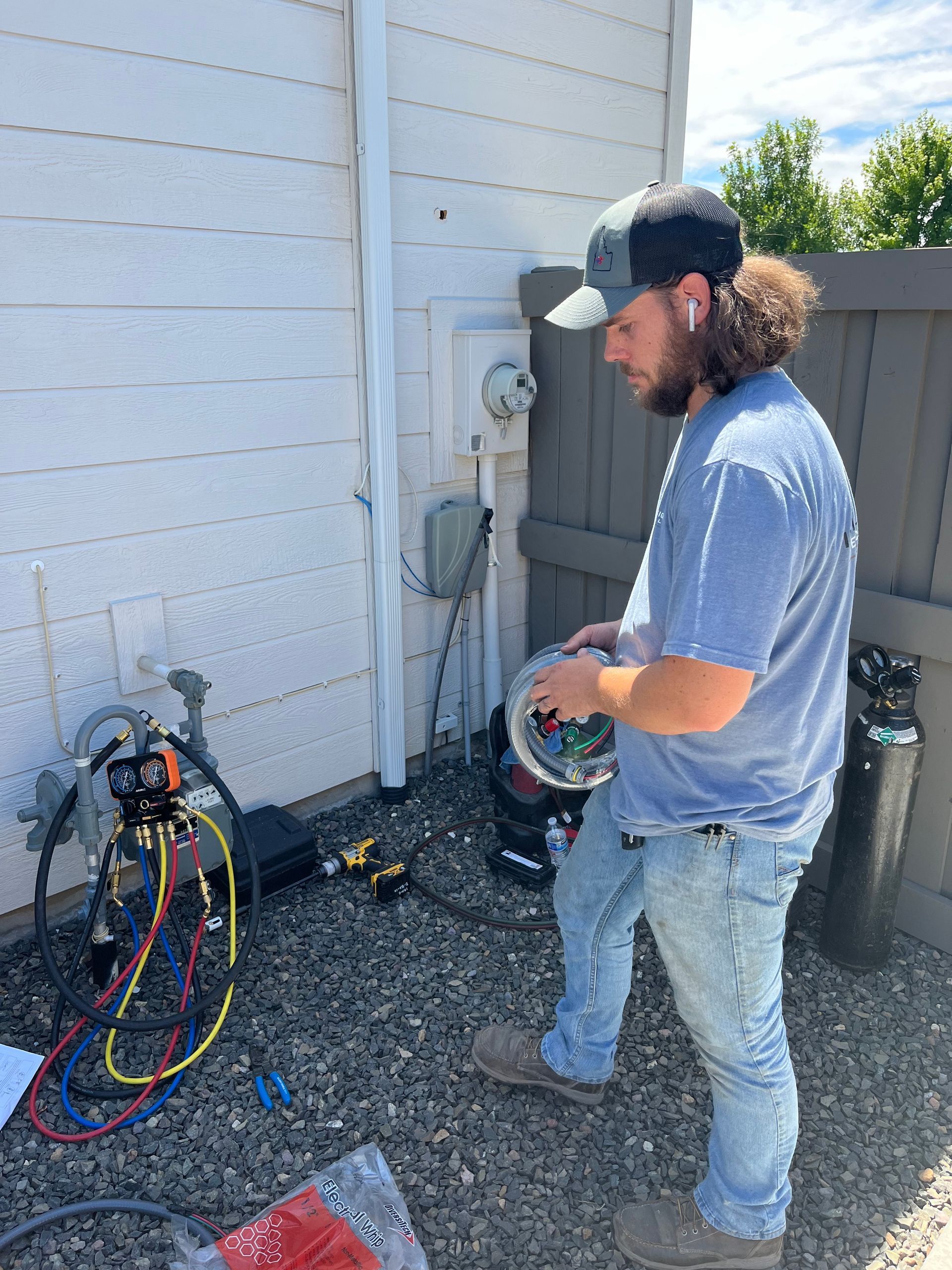 Technician holding cables beside outdoor HVAC equipment and a white building wall
