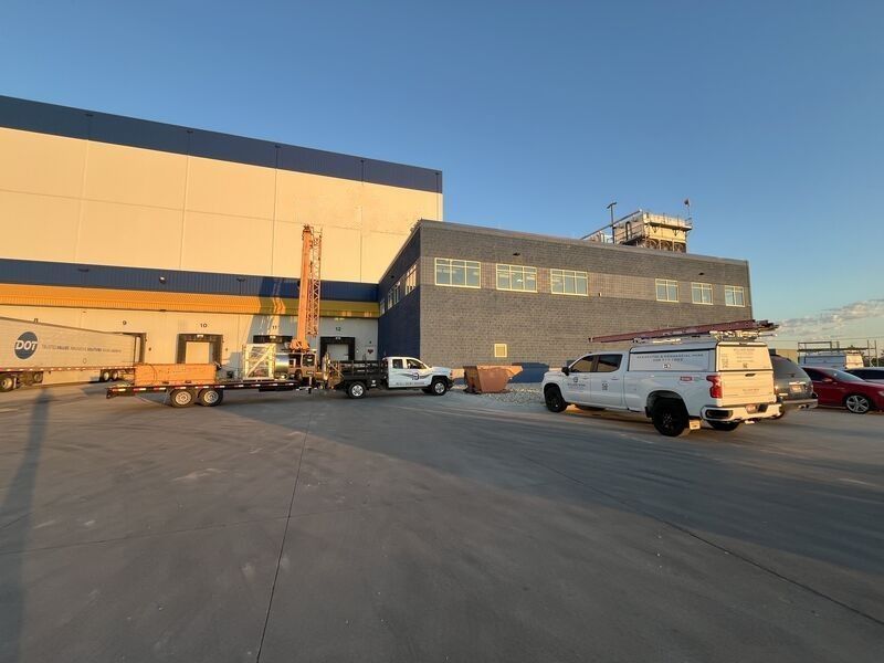 Industrial warehouse exterior at sunset with parked trucks and vans on a wide concrete lot