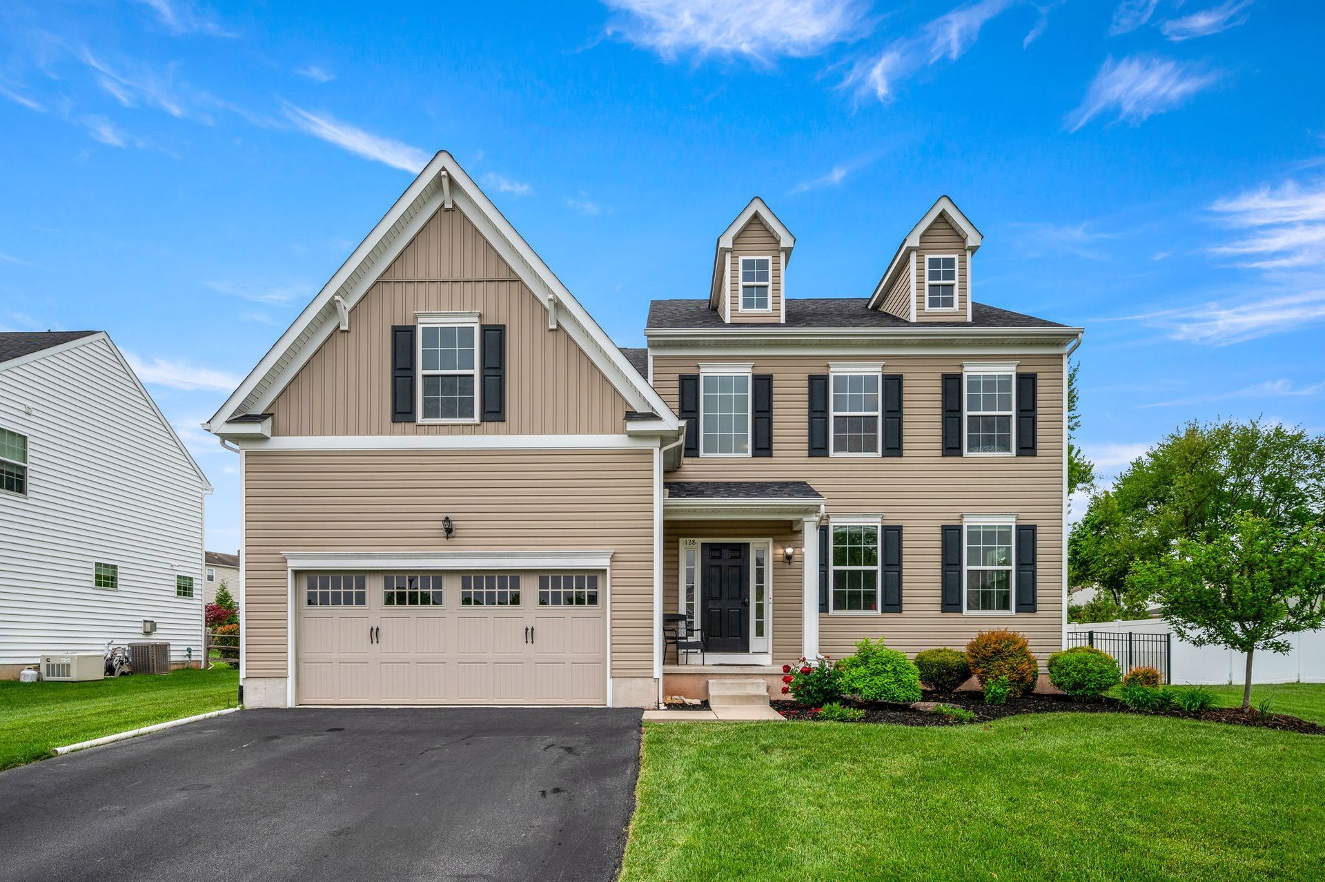A large tan house with black shutters and a large garage.
