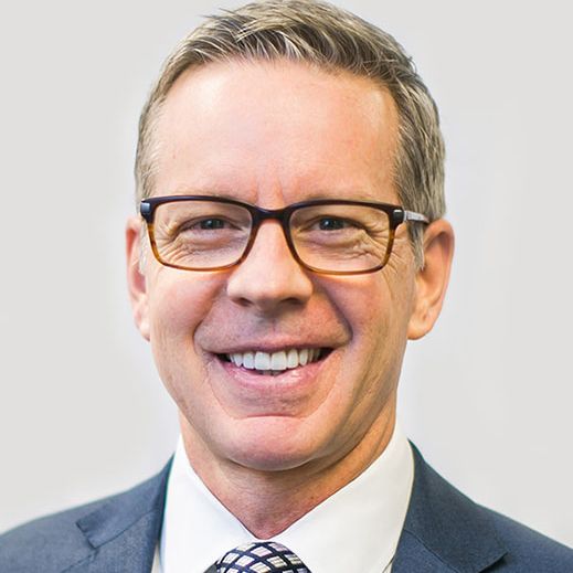 A man wearing glasses and a suit and tie is smiling.