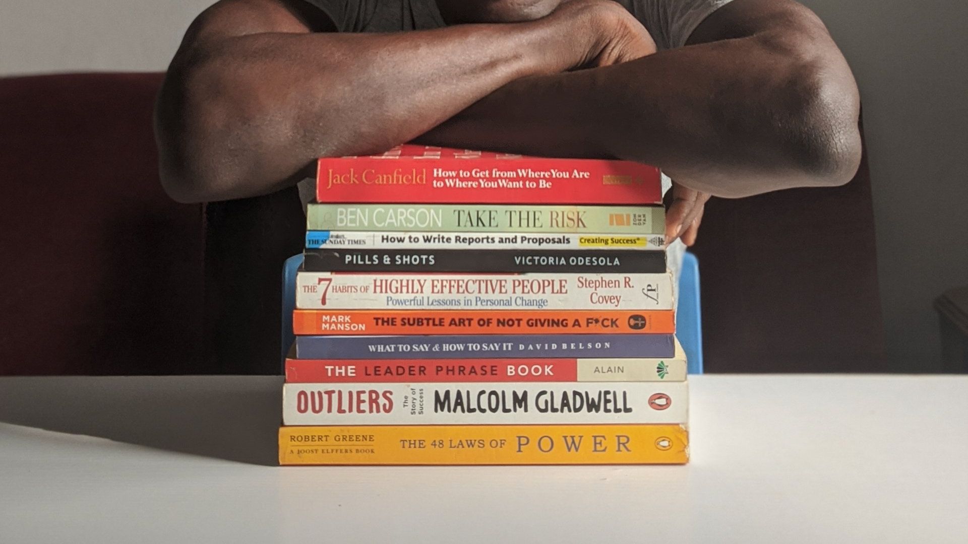 A man is holding a stack of books including one by malcolm gladwell