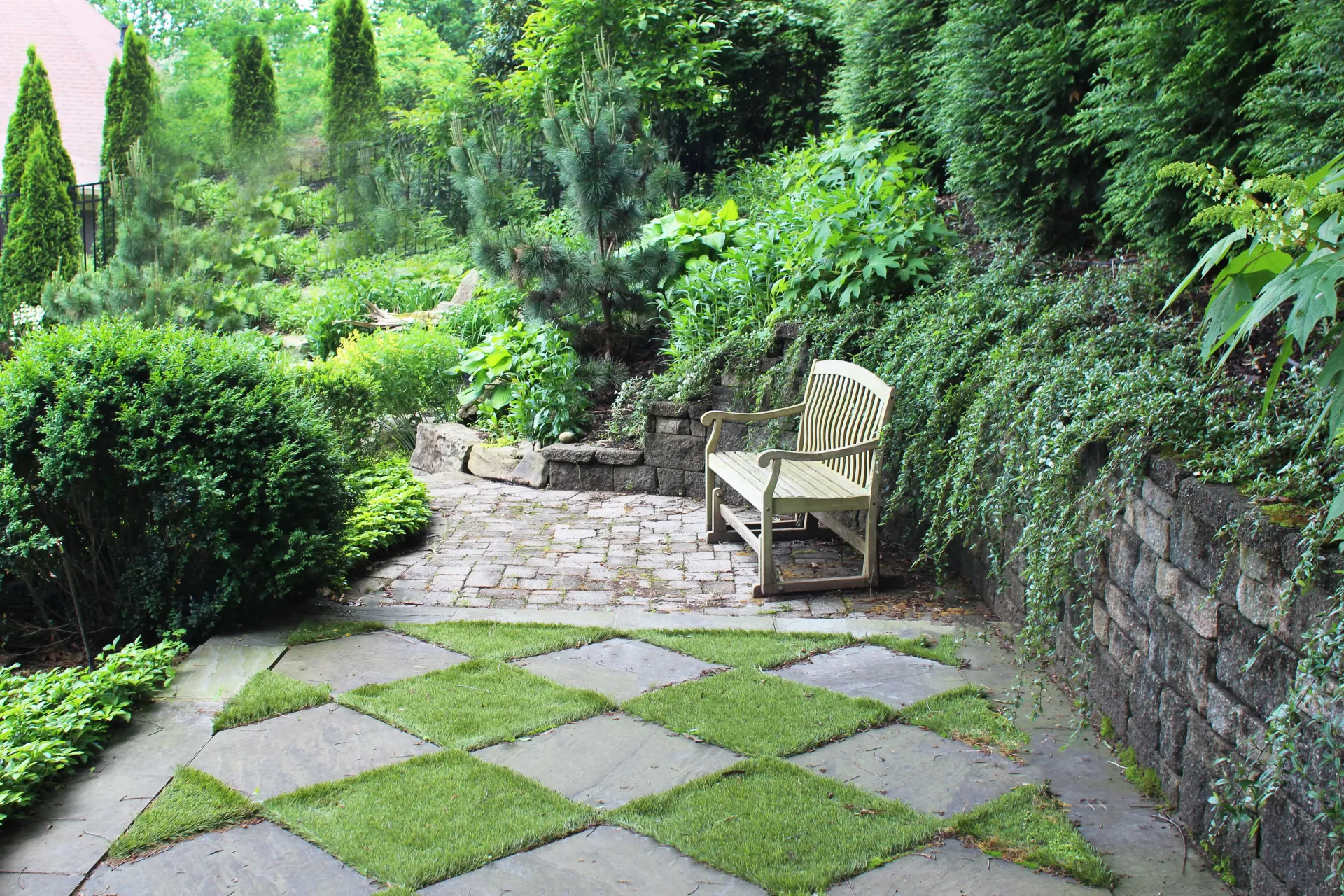 Garden patio with stone pavers, lush greenery, and a wooden bench along a wall