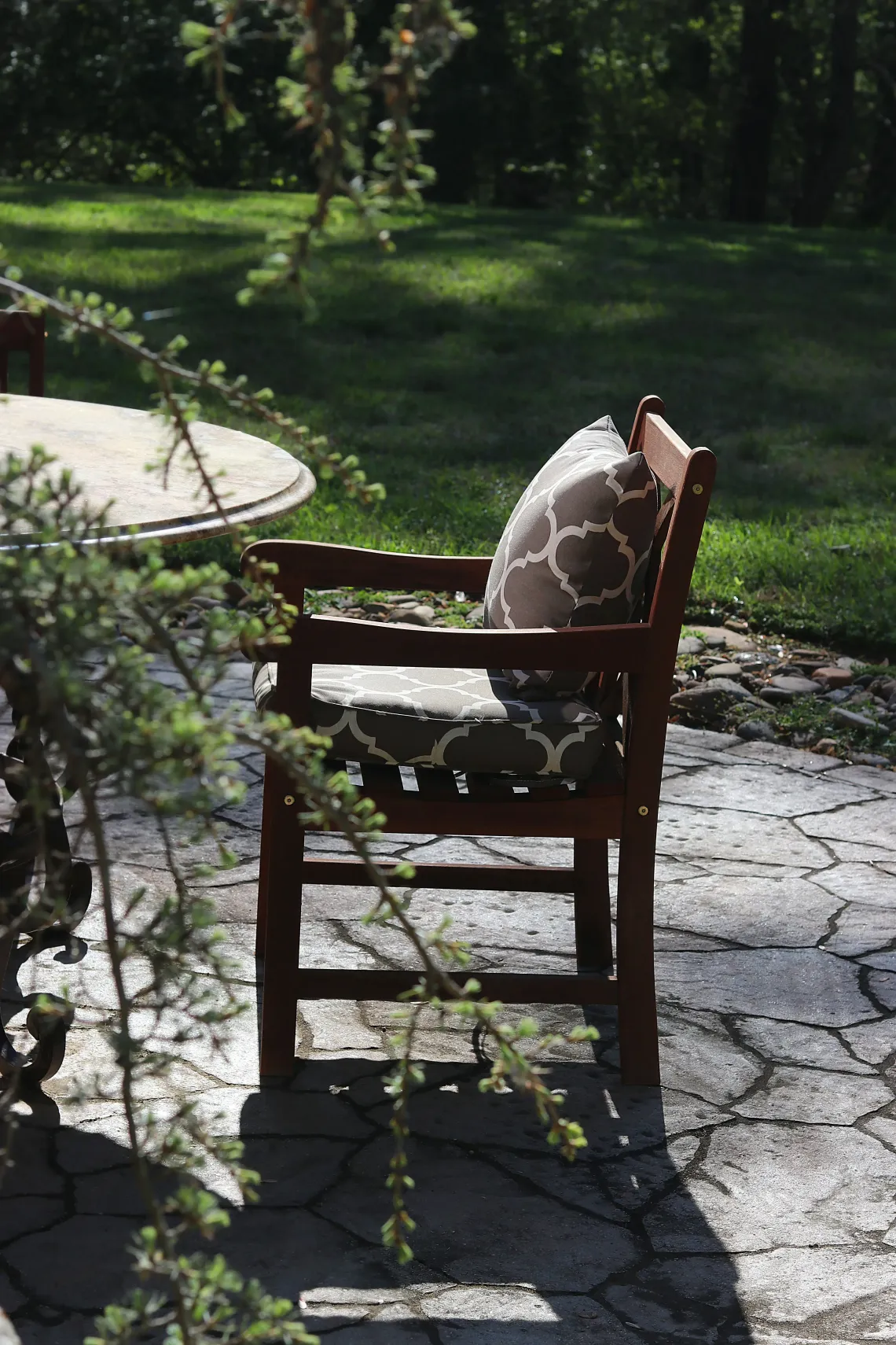 Wooden chair with patterned cushion on a sunlit patio beside a garden path