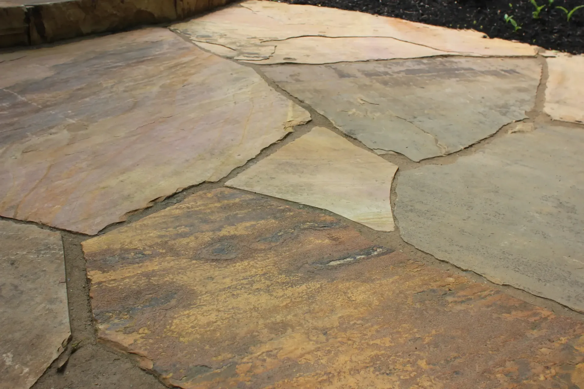 Stone-paved patio with irregular tan and brown flagstones in sunlight