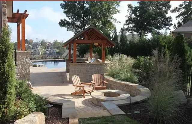 Stone patio with wooden chairs beside a small pool, pergola, and landscaped garden by the water