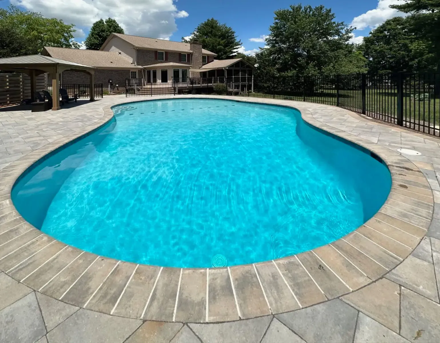 Backyard swimming pool with blue water, stone deck, and house in the background