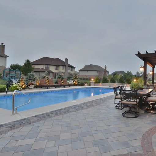 Poolside patio with lounge chairs and tables beside a long swimming pool at dusk