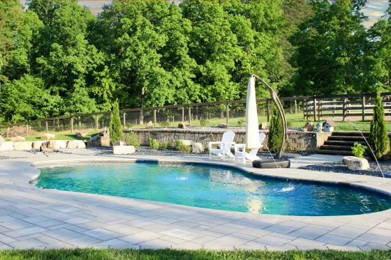 Outdoor pool with turquoise water, stone deck, fountain, and lush green trees in the background