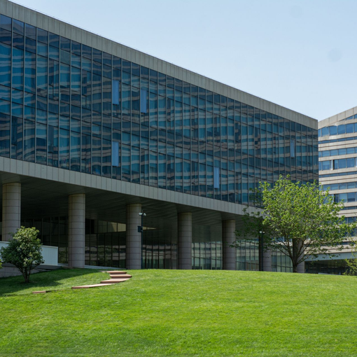 Modern glass office building with a large green lawn and trees in front
