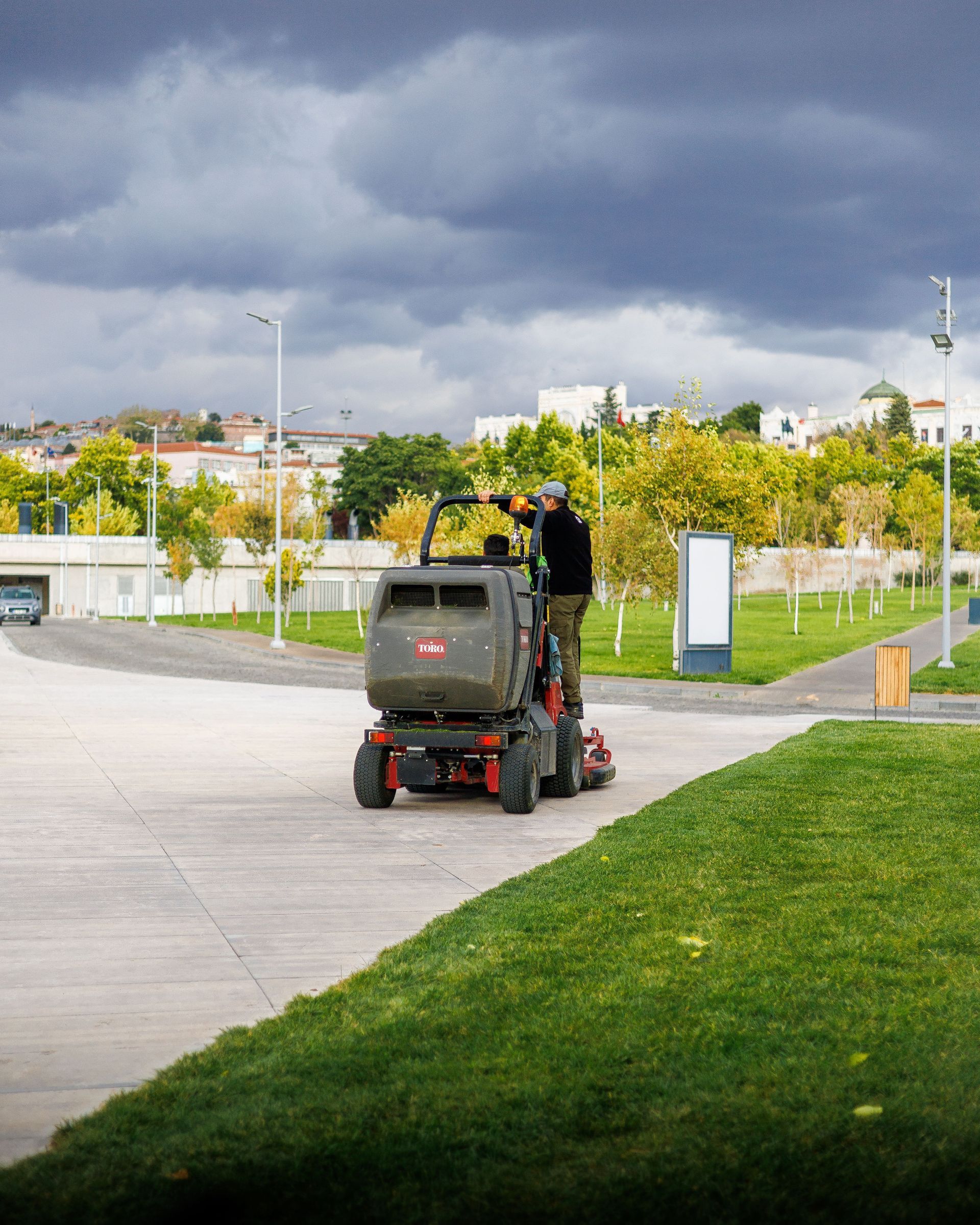 Person riding a red mobility scooter on a paved path near grass and a fence under dark clouds