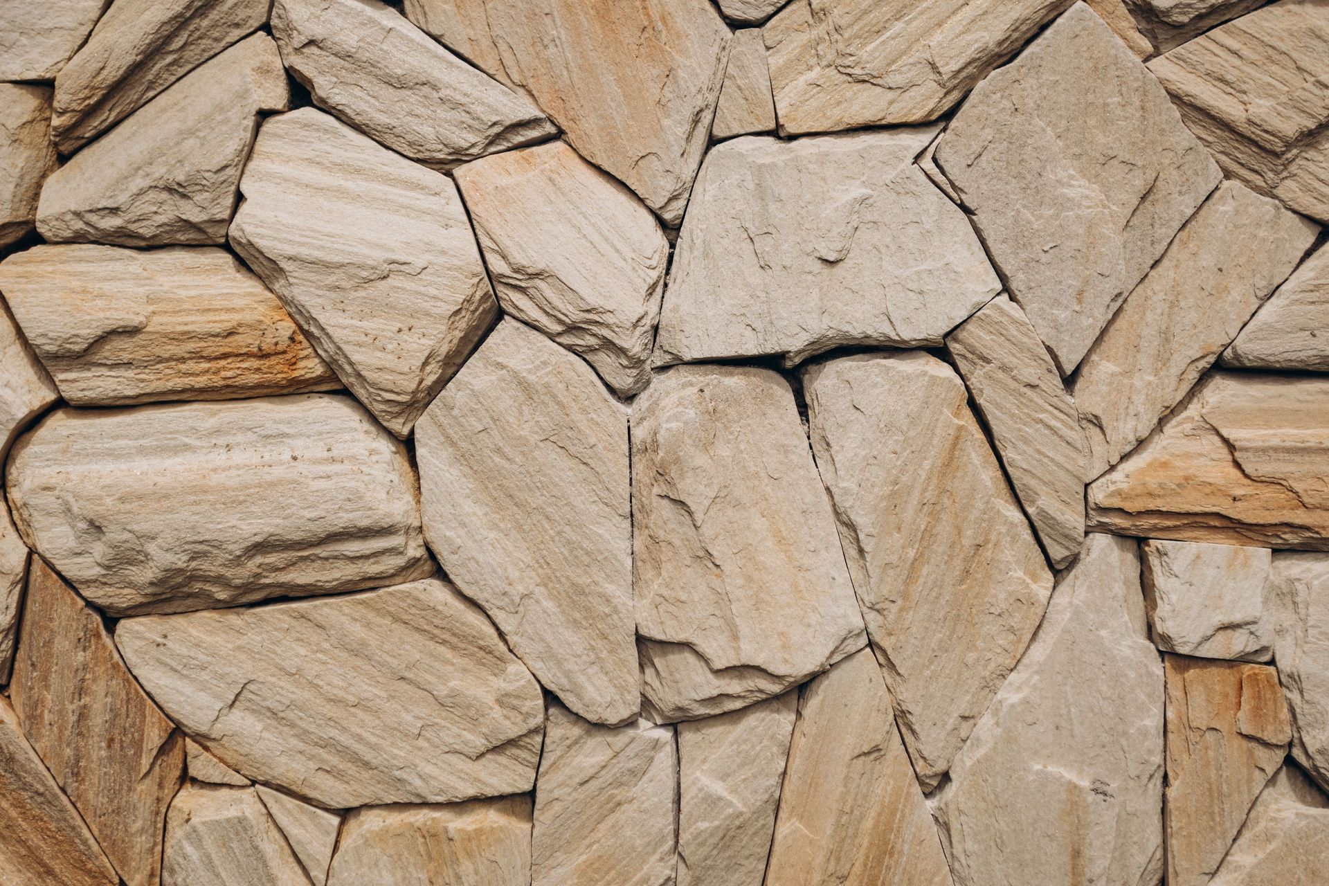 Close-up of tan and beige stacked stone wall with irregular textured blocks