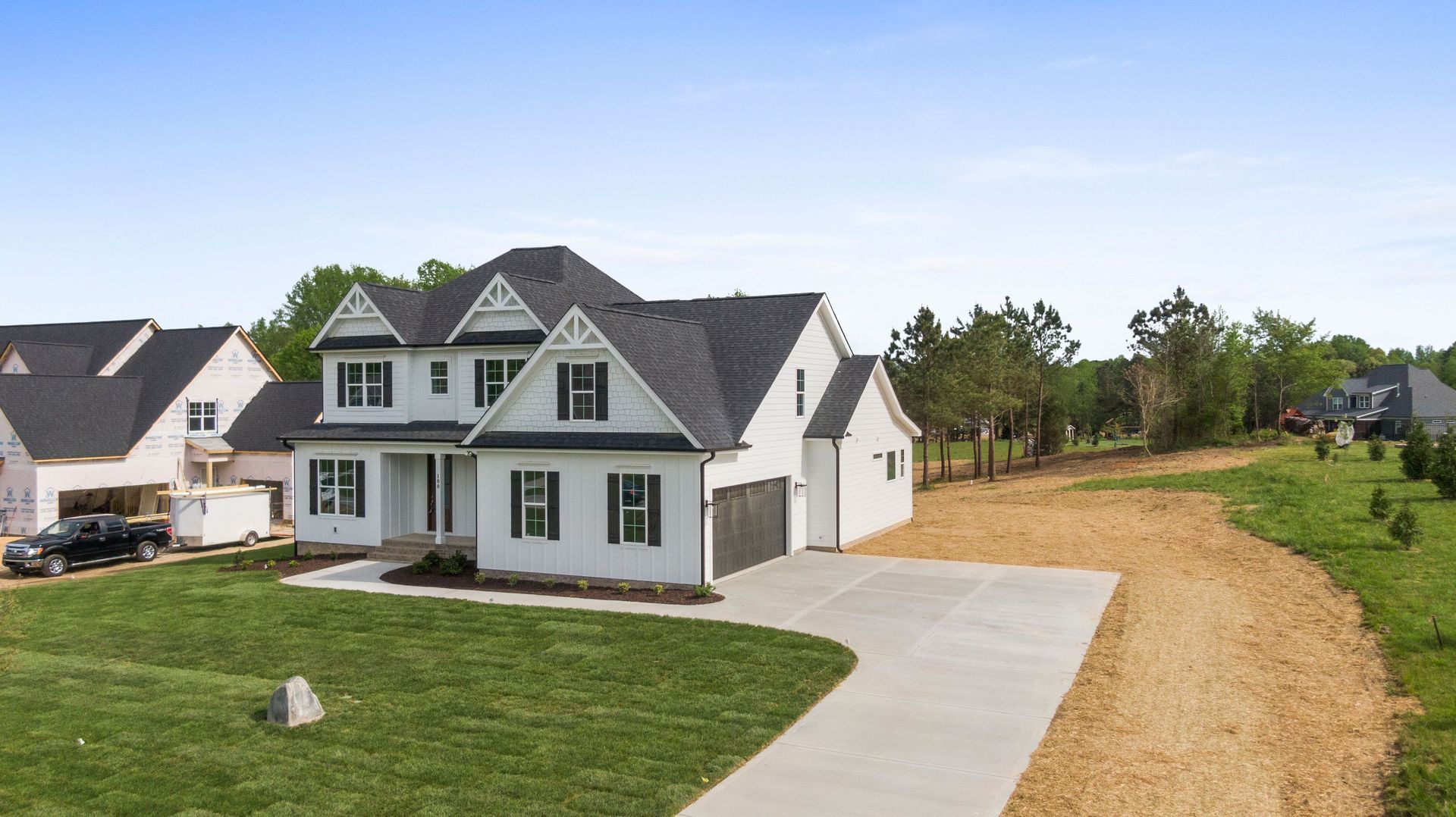 Suburban house with white siding, front lawn, driveway, and a wooded lot beside it