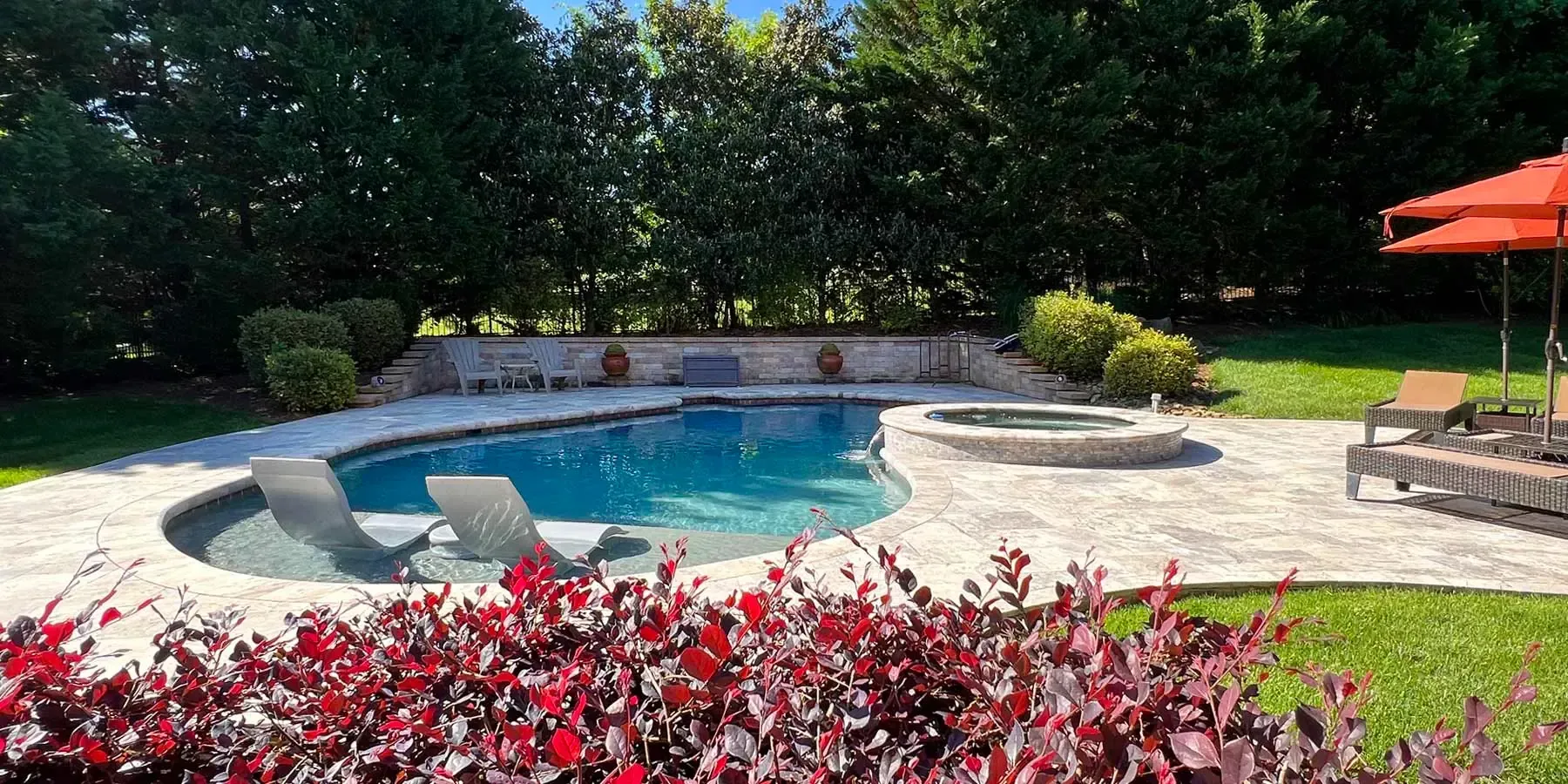 Backyard pool with lounge chairs, red flowers, and an orange umbrella under bright sunlight