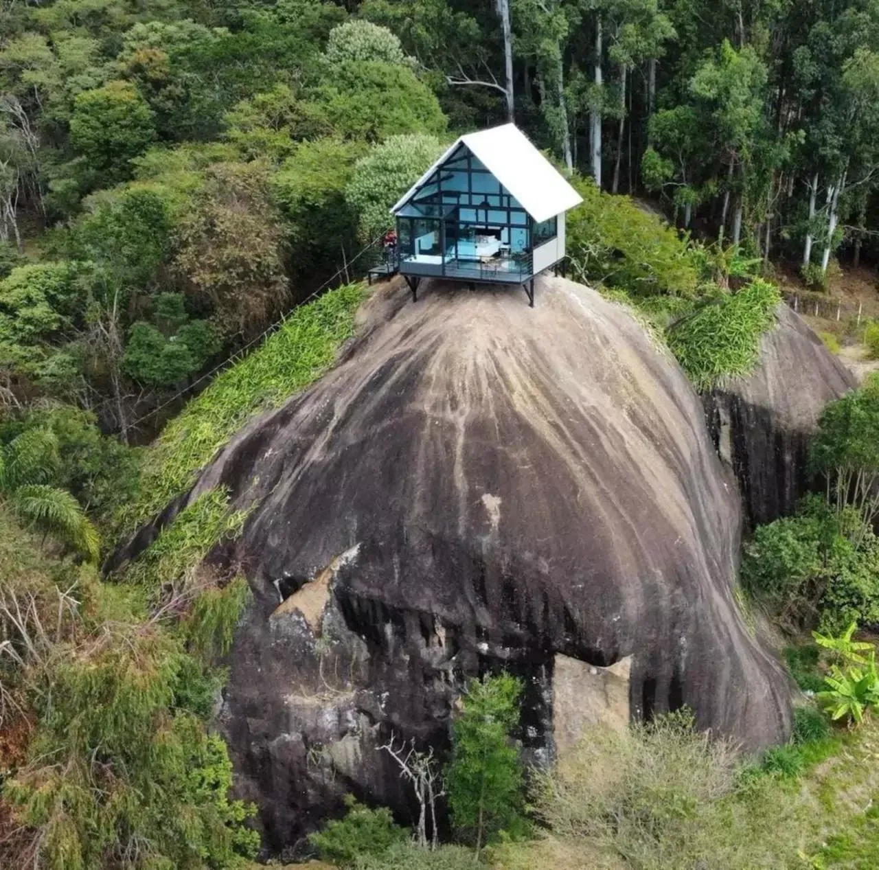 Uma pequena casa fica no topo de uma grande rocha no meio de uma floresta. Chalé Pedra Negra