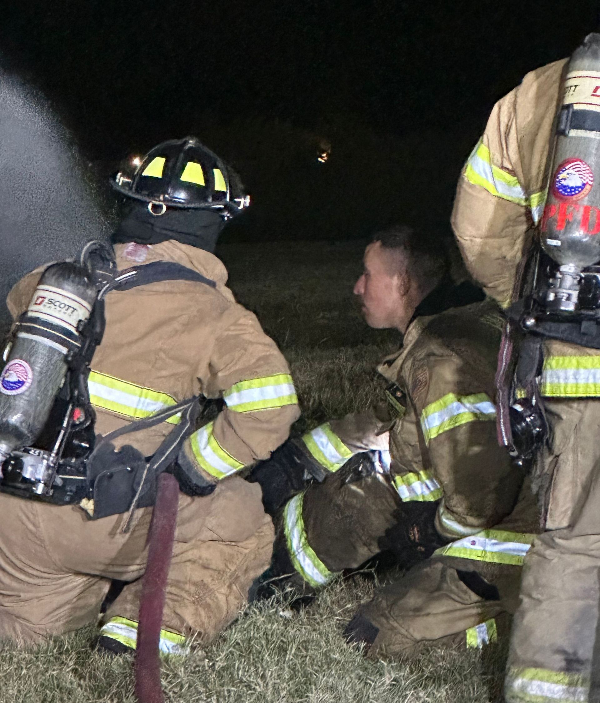 A group of firefighters are kneeling down in the grass